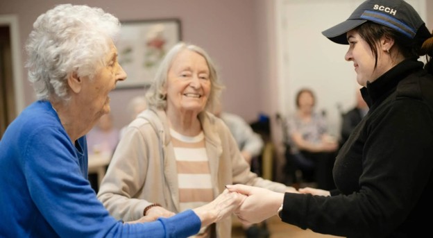 Elderly woman dancing with caregiver in a senior living community.